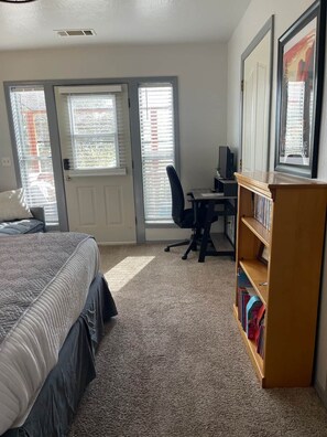 A bedroom with a bed, a desk, a chair, a bookshelf, and a door leading to a balcony.