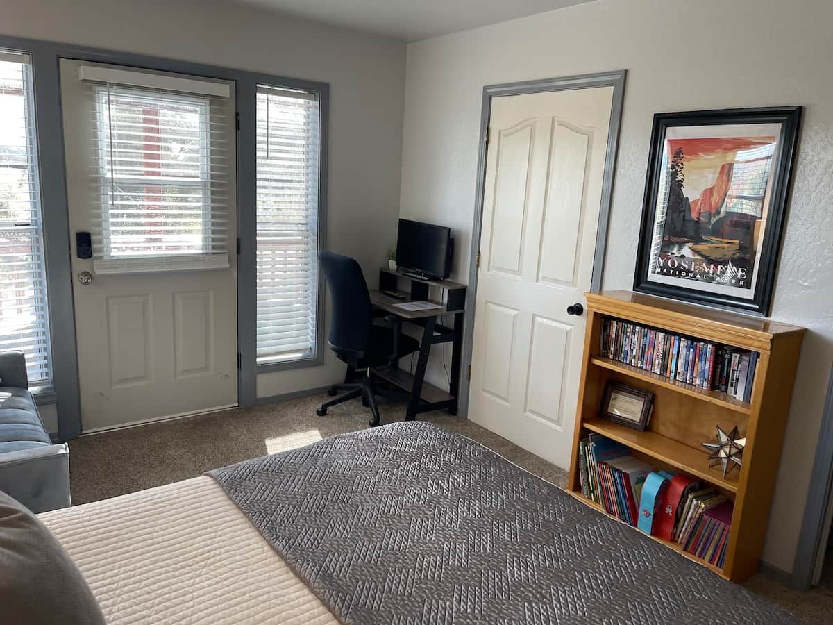 A bedroom with a bed, a desk, a chair, a bookshelf, and a door.