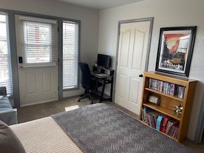 Un dormitorio con cama, escritorio, silla, estantería y una puerta.