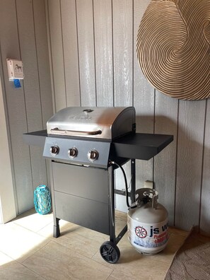 A portable grill with a gas tank on a wheeled cart, set against a wooden wall. - The Restoration Hideaway (Ahwahnee)