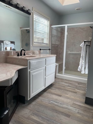 A bathroom with a vanity, a shower, and a large mirror.
