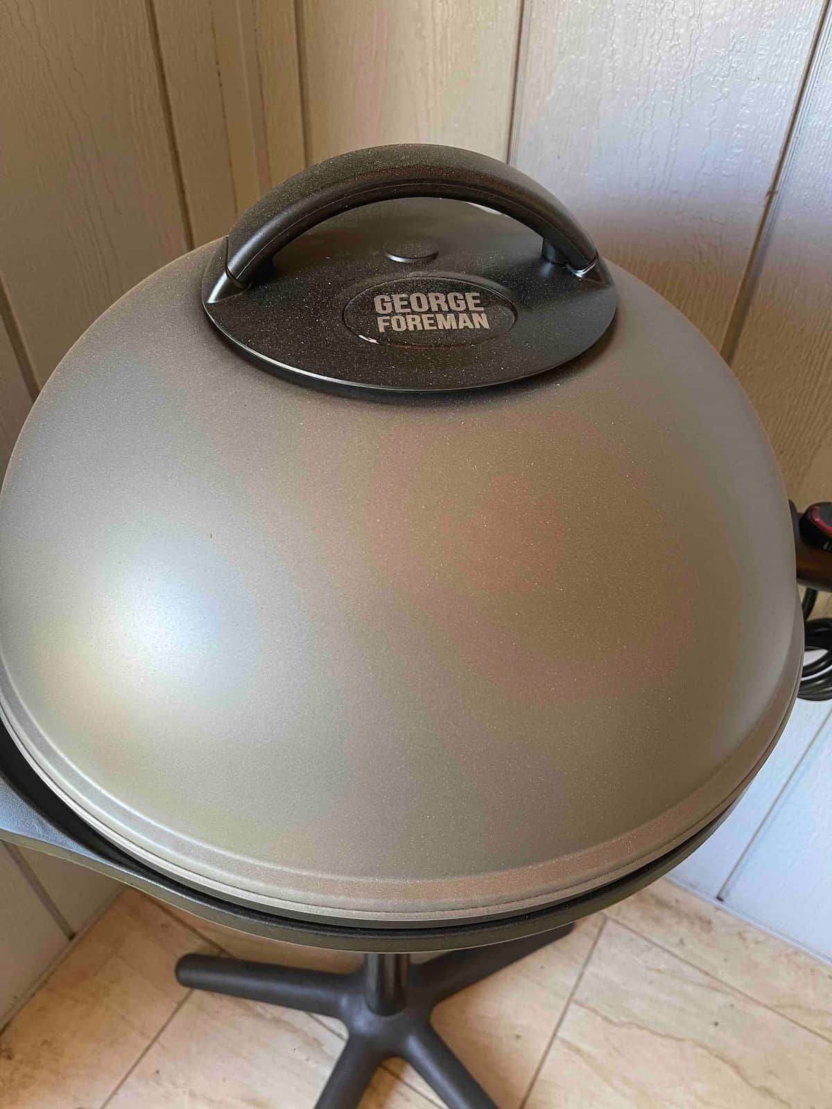 A George Foreman grill with a black handle and lid, placed on a metal stand.