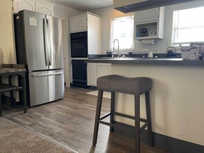A modern kitchen with a stainless steel refrigerator, a built-in oven, and a bar area with a stool.