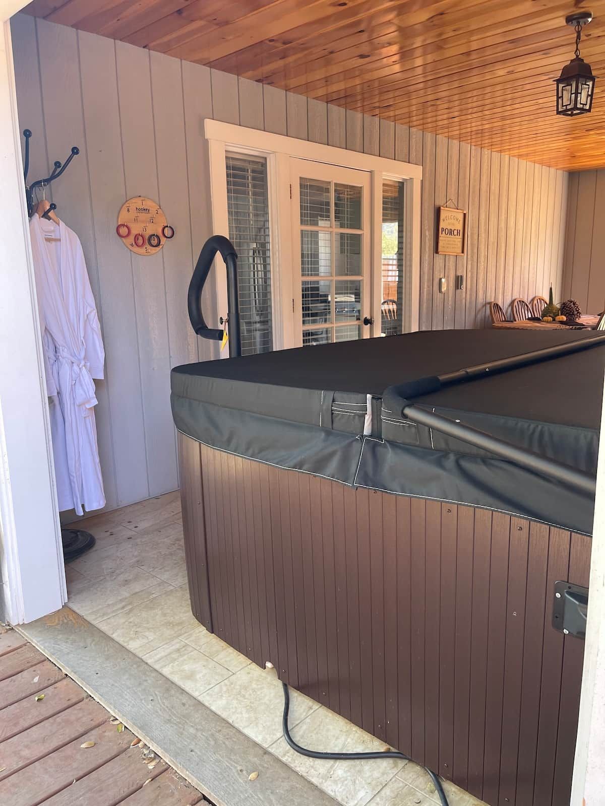 A spa area with a hot tub, wooden walls, a door, and a towel rack with a robe.