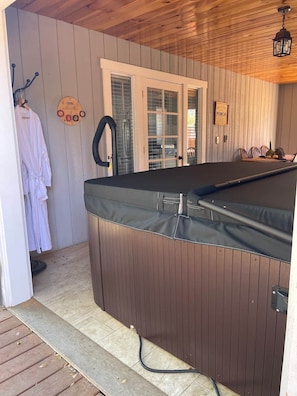 Zona de spa con hidromasaje, paredes de madera, una puerta y un perchero con bata.
