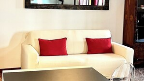 A modern living room with a white sofa, red cushions, a glass coffee table, and a large woven light fixture. - Canal View (Venezia)