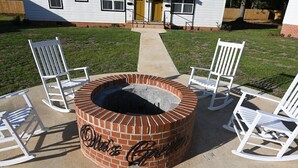 A circular brick fire pit with the words "Ollie's Garden" on it, surrounded by white rocking chairs.