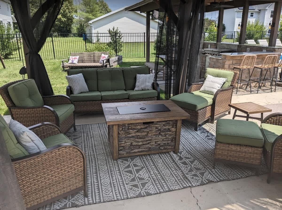 An outdoor patio with wicker furniture, a stone coffee table, and a patterned rug.