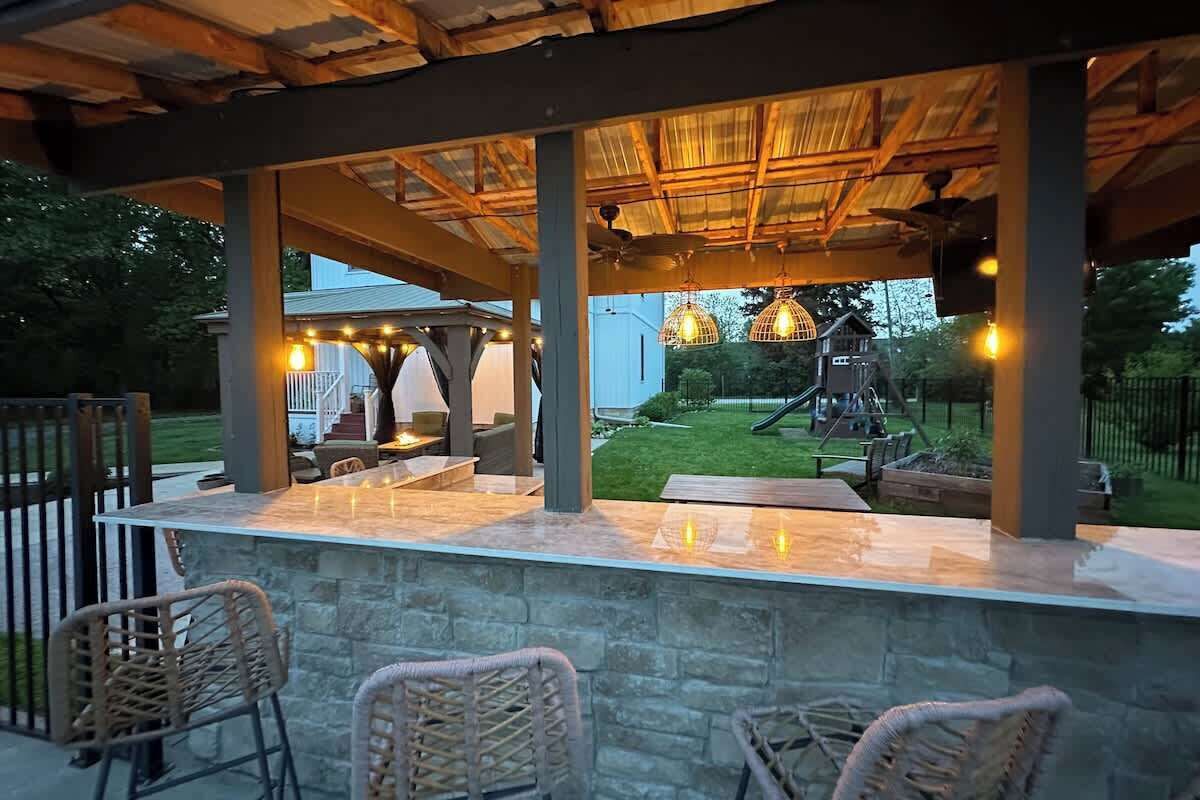 Une terrasse extérieure avec des sièges en pierre, une pergola en bois et des guirlandes lumineuses.