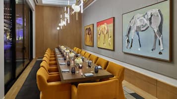 A long conference table with yellow chairs, set with glassware and a centerpiece, in a modern room with artwork on the walls.