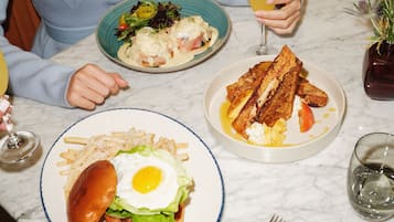 A dining table with plates of food, a glass of orange juice, and a fork and knife.