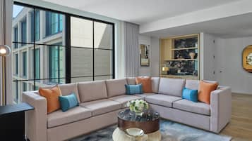 Una sala de estar moderna con un sofá seccional, una mesa redonda de centro y un amplio ventanal que ofrece vistas a un edificio.