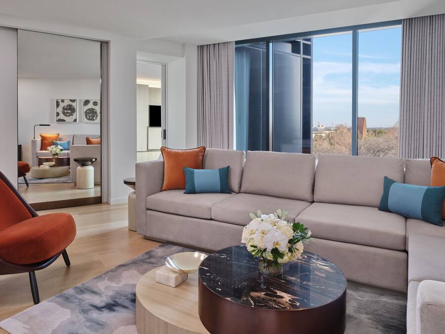 Ett modernt vardagsrum med en beige soffa, en orange fåtölj och ett runt soffbord med en vas med blommor.