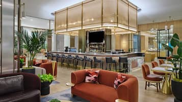 A modern hotel lobby with a bar area, seating arrangements, and a large plant.
