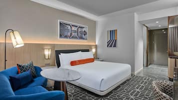 A hotel room with a bed, a round table, a blue armchair, and a wall-mounted artwork.