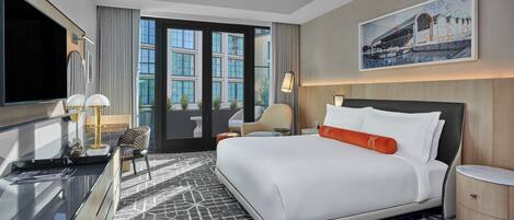 Habitación de hotel moderna con una cama grande, un escritorio con televisor de pantalla plana, una silla y un ventanal con vistas a la ciudad.