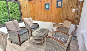 Un patio con mobiliario de mimbre, una mesita y cuadros en la pared.