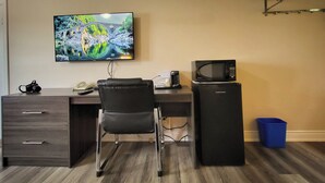 Un espacio de oficina funcional con escritorio, silla y refrigerador. Un televisor montado en la pared muestra una imagen panorámica.