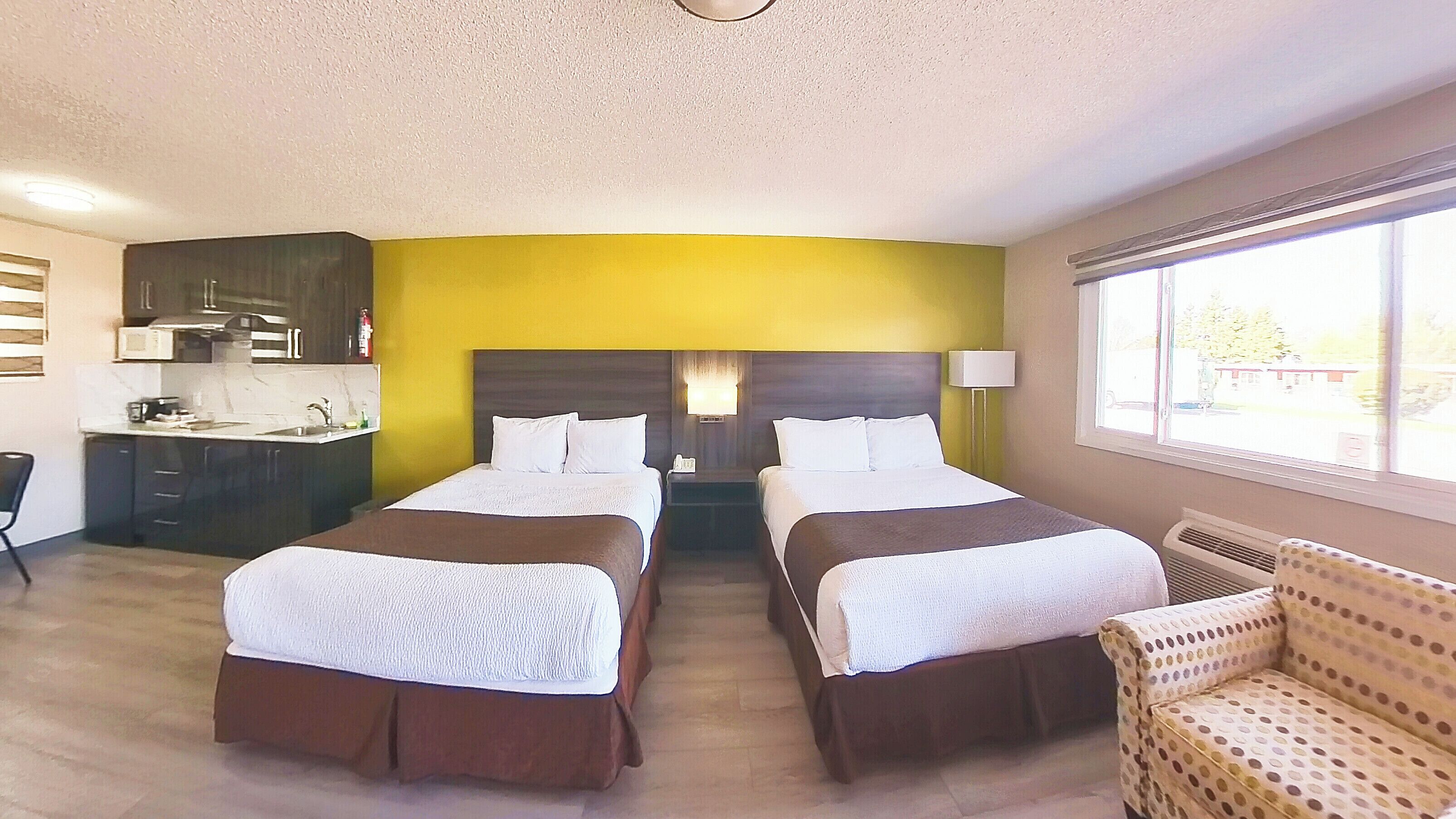 A hotel room with two beds, a kitchenette, a sofa, and a window with a view.