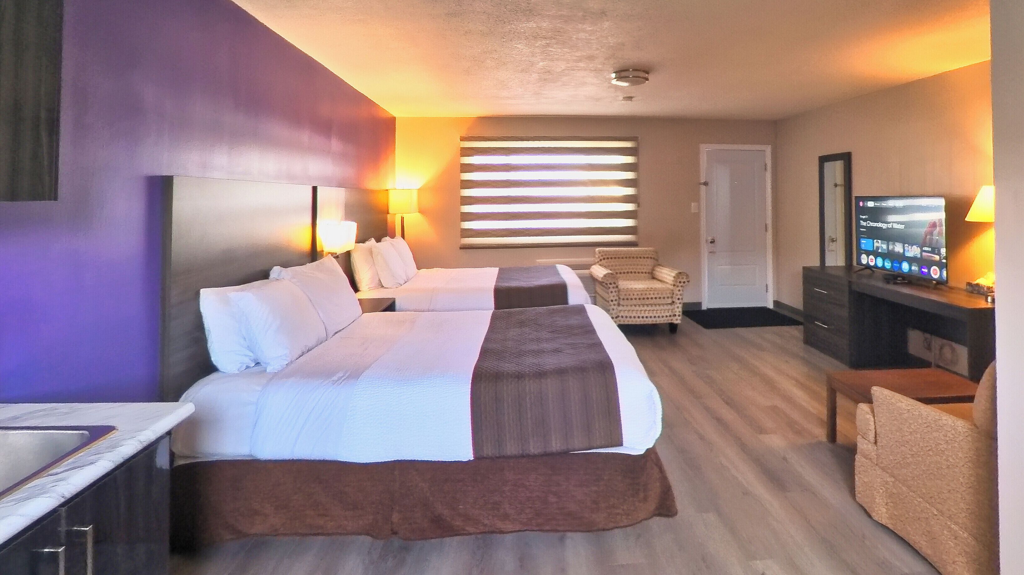 Ein Hotelzimmer mit zwei Betten, einem Schreibtisch, einem Stuhl, einem Fernseher und einem Fenster mit Jalousien.