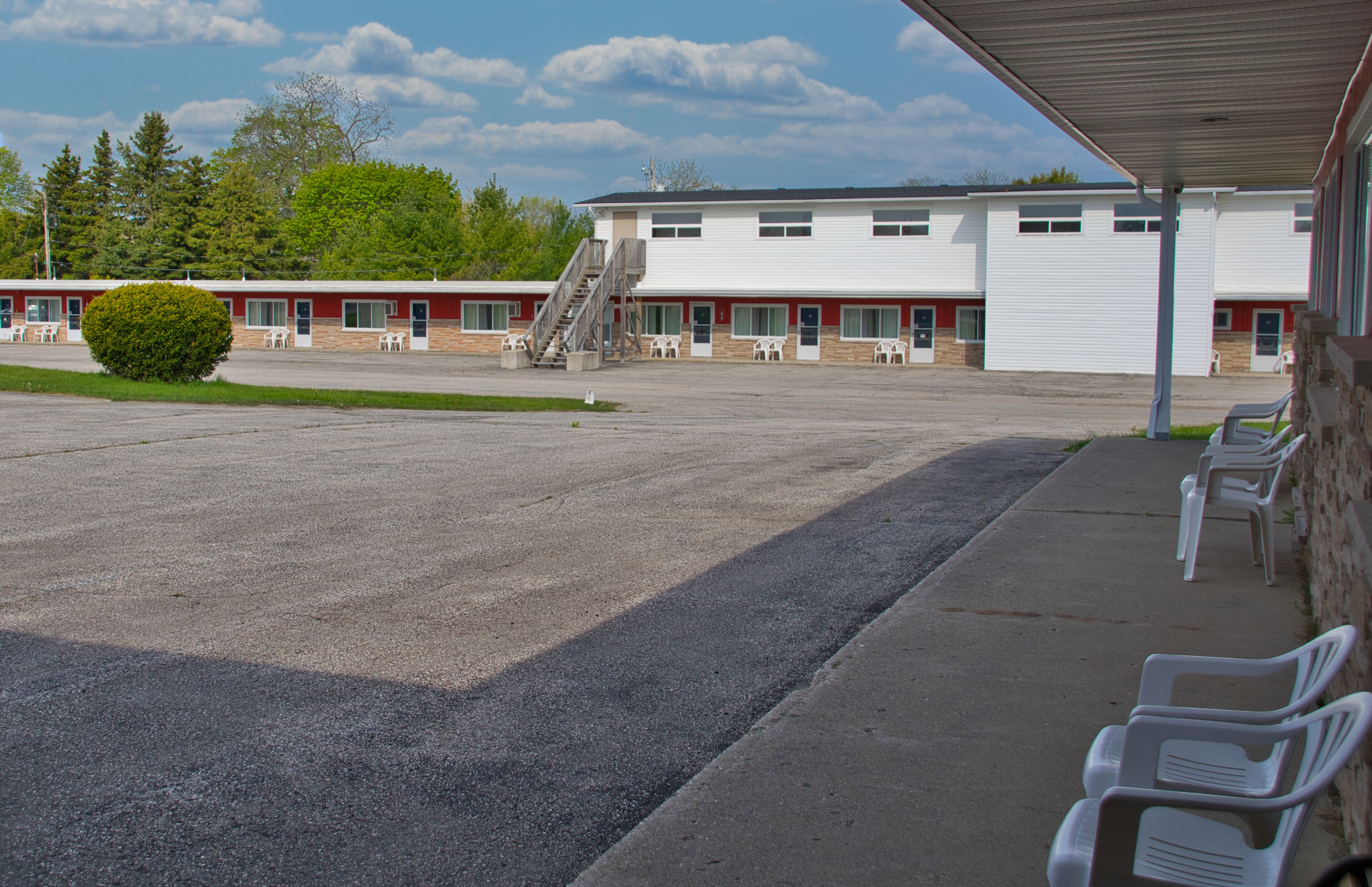 A motel with a covered parking area, outdoor seating, and a large building with multiple windows and a garage door.