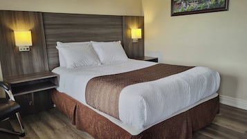 Relax in comfort with a neatly made bed, a wooden headboard, and a cozy chair at the foot.