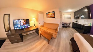 Habitación de hotel con televisión, sofá, escritorio, lámpara y zona de cocina.