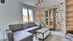 A modern living room with a grey sectional sofa, a wooden cabinet with glass doors, and a small table with a vase of flowers.