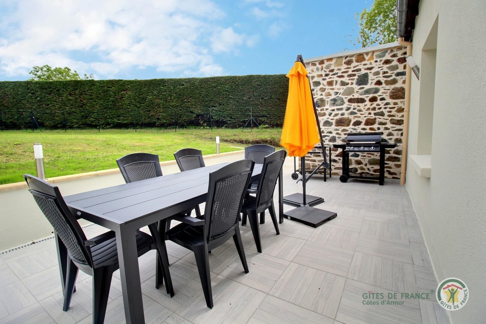 Een buitenpatio met een tafel, stoelen, een barbecue en een stenen muur.