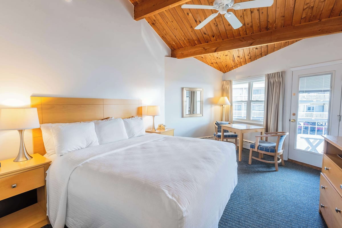 A hotel room with a large bed, two bedside tables with lamps, a desk with a chair, and a window with curtains.