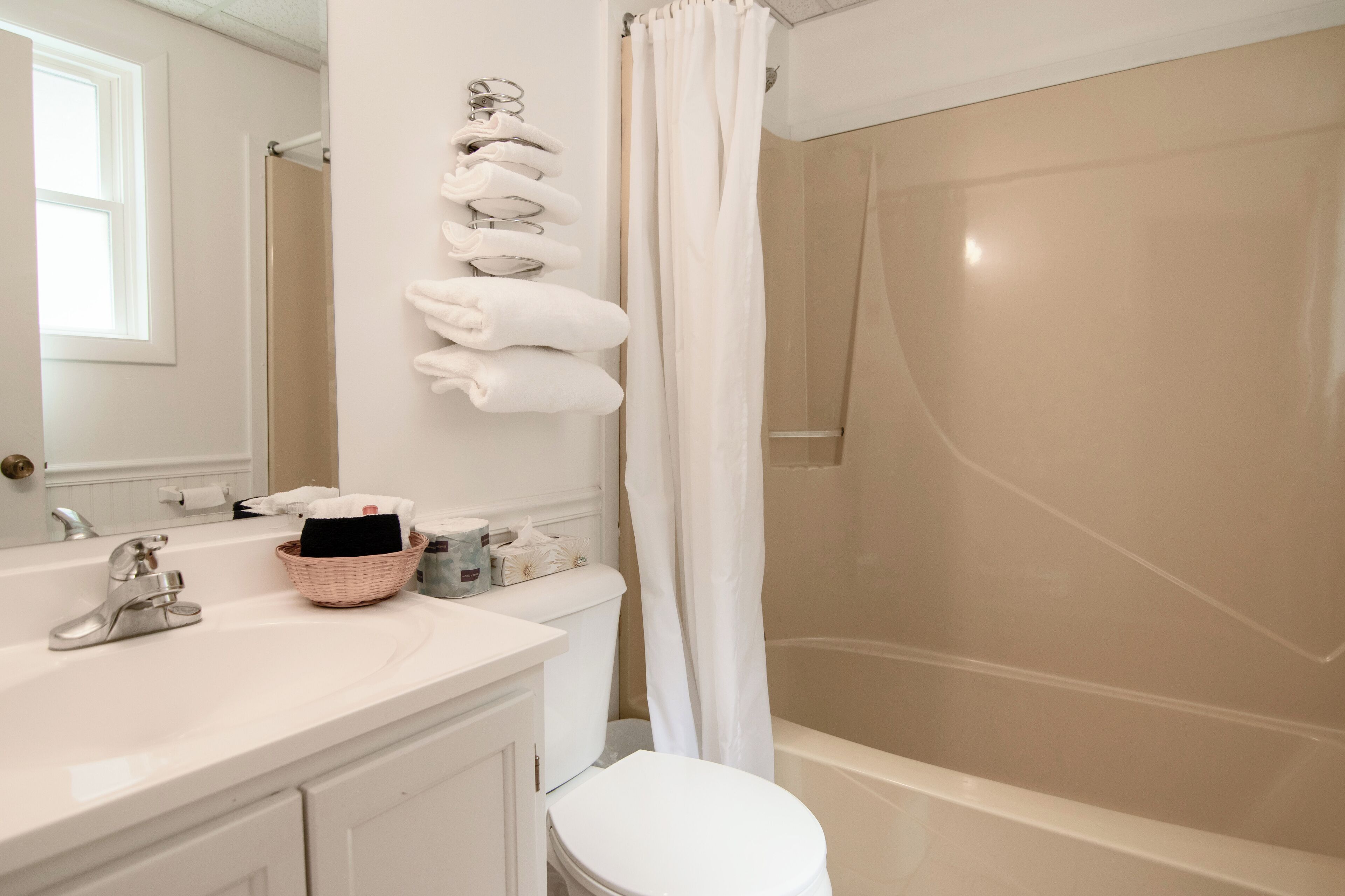 A bathroom with a white sink, a toilet, a shower with a glass door, and a towel rack with multiple towels.