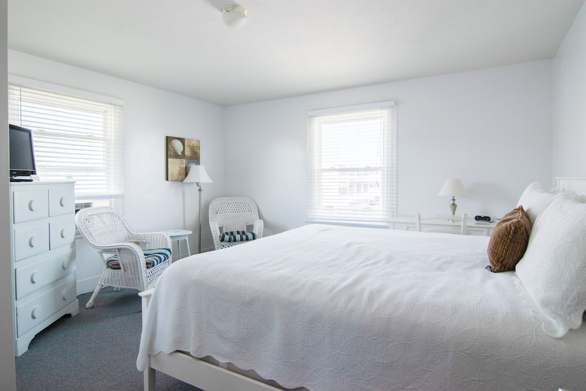 A bedroom with a bed, two chairs, a dresser, and a television.