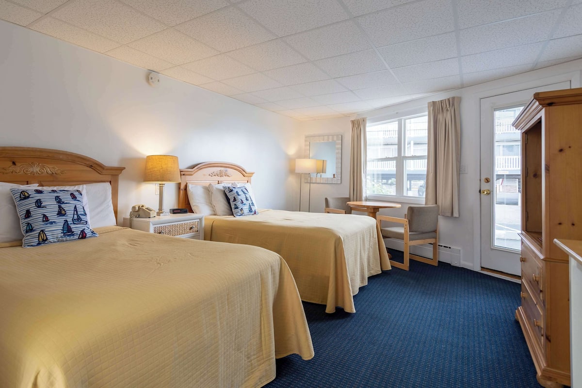 A hotel room with two beds, a desk, a chair, a wardrobe, and a window with curtains.