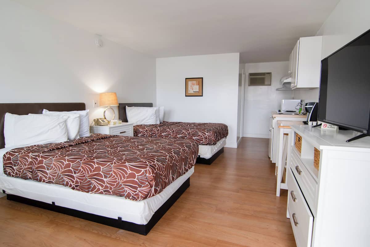 A hotel room with two beds, a desk with a TV, a microwave, and a small kitchenette.