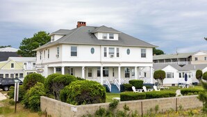 A two-story white house with a porch, a small staircase, and a fenced yard with outdoor seating. - The Gull Oceanside Inn & Motel  (Old Orchard Beach)