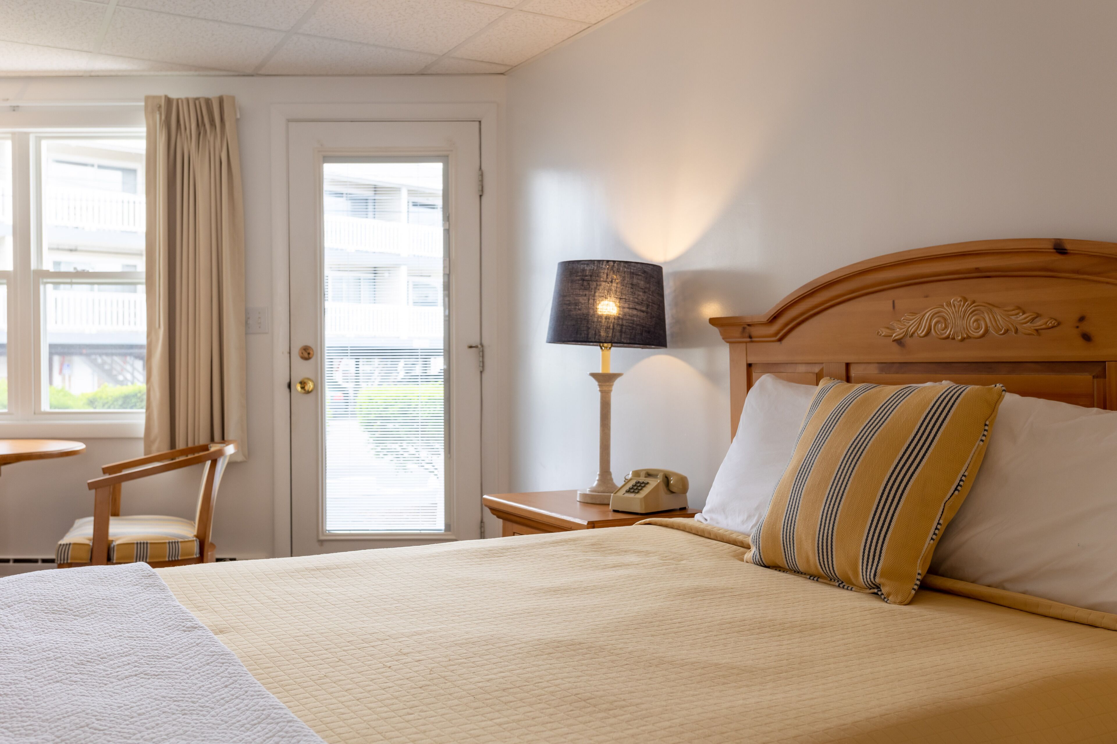 A hotel room with a bed, a nightstand with a lamp, a chair, and a window with curtains.