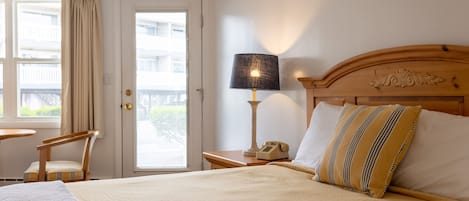 A hotel room with a bed, a nightstand with a lamp, a chair, and a window with curtains.