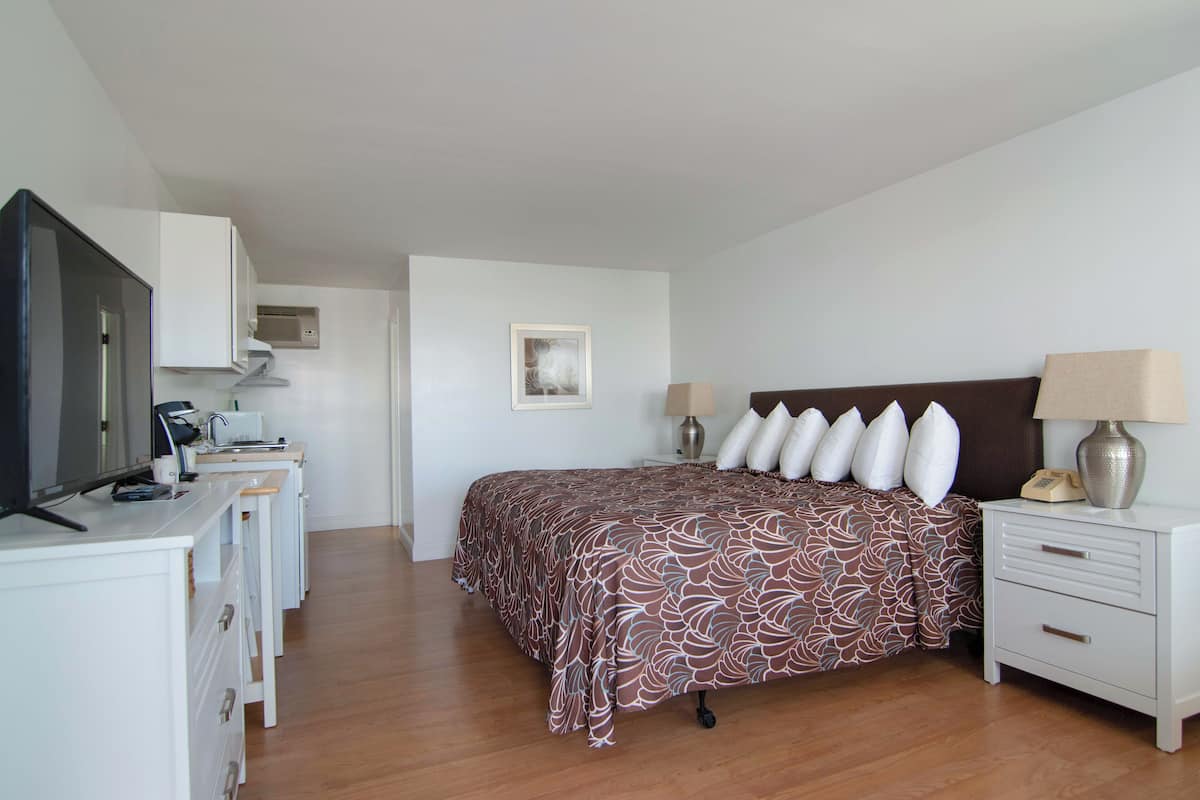 A bedroom with a bed, bedside tables, a desk, a television, and an air conditioning unit.