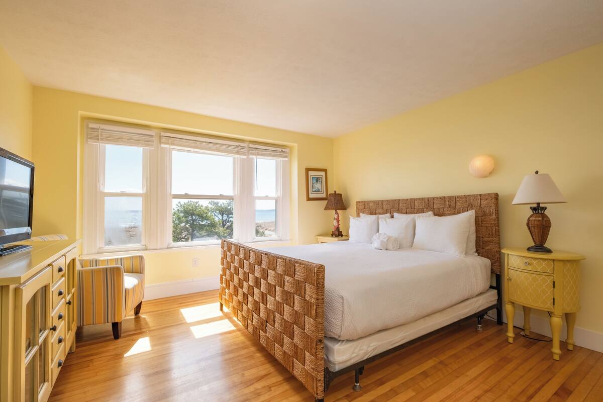 A bedroom with a bed, a television, a window with a view, a lamp, and a bedside table.