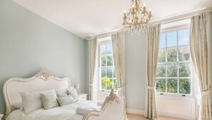 A bedroom with a large bed, a chandelier, and large windows with curtains. - 3 bedroom accommodation in Cromer (Cromer)