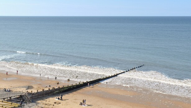 A beach with a long wooden jetty extending into the sea, people walking along the shore, and a clear sky. - 3 bedroom accommodation in Cromer (Cromer)