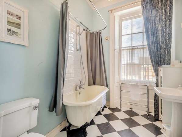 A bathroom with a white bathtub, a toilet, and a window with curtains.