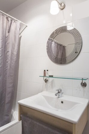 Een badkamer met een witte wastafel, een glazen plank, een ronde spiegel en een douchegordijn.