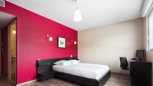 Ein modernes Schlafzimmer mit roter Akzentwand, einem Bett, einem Schreibtisch mit Computer und einem Fenster.