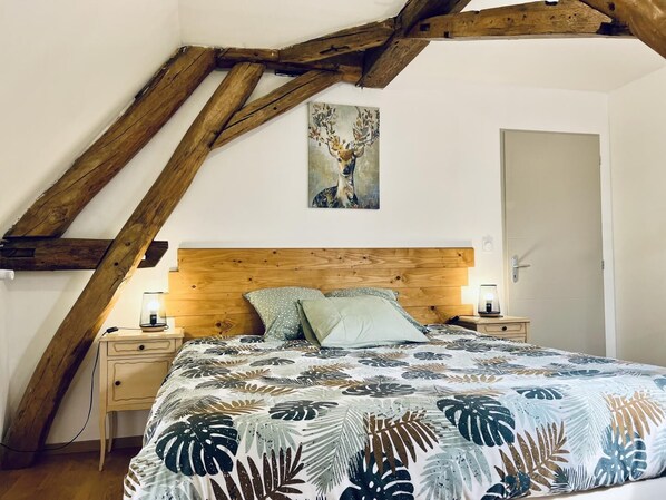 A bedroom with a wooden ceiling, a bed with a floral bedspread, two bedside lamps, and a painting on the wall.