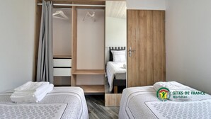 Une chambre avec deux lits, une armoire en bois et un miroir.
