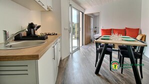 Une cuisine moderne avec un plan de travail en bois, un évier en acier inoxydable et une machine à café. On y trouve également un coin repas avec une table pour quatre personnes, agrémentée de chaises noires et d’un coussin rouge.