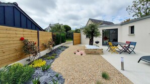 Un patio extérieur moderne avec un chemin de gravier, une clôture en bois et un petit espace jardin agrémenté de plantes et de fleurs.