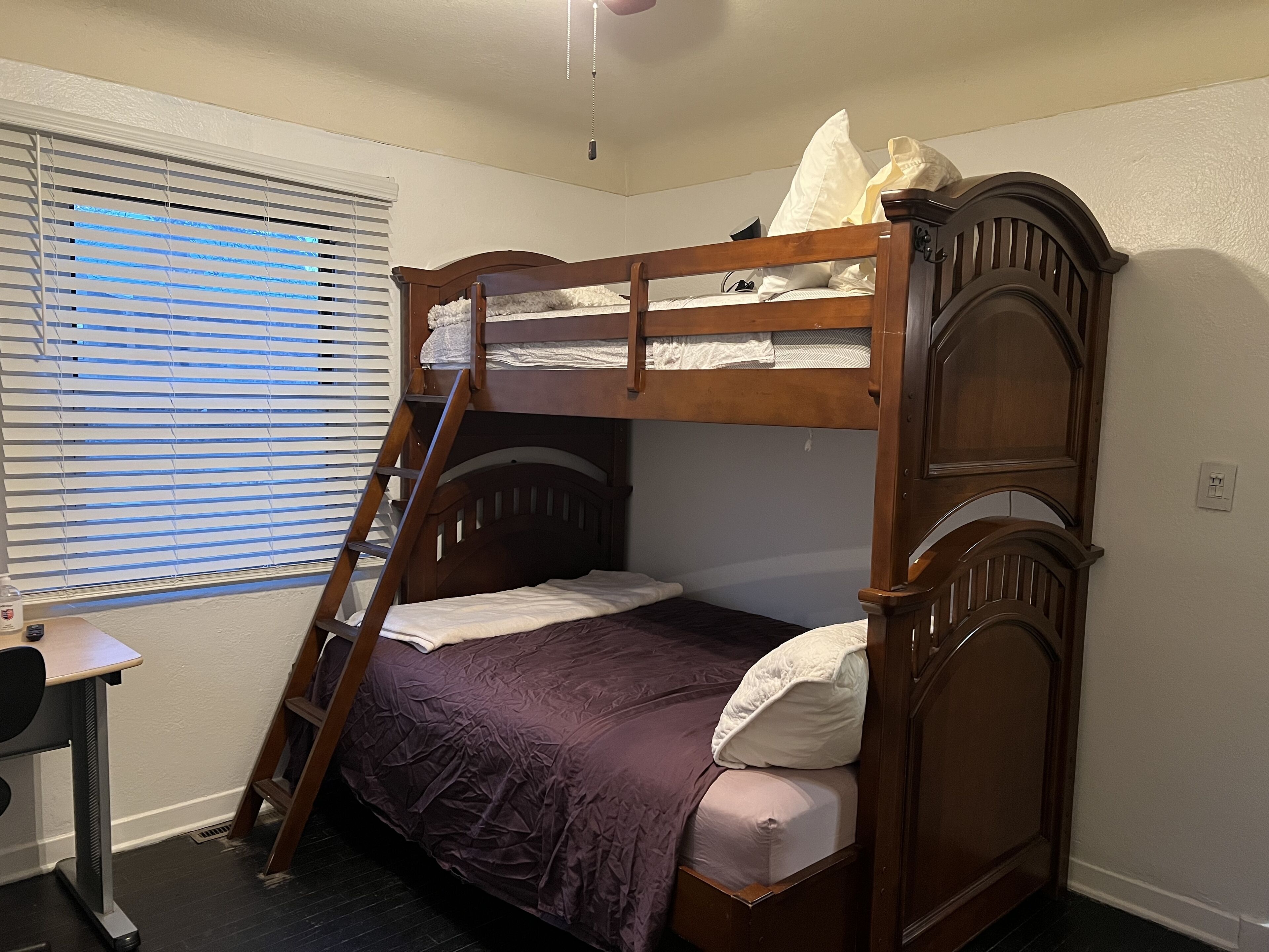 A bunk bed with a ladder, a desk, and a window with blinds.