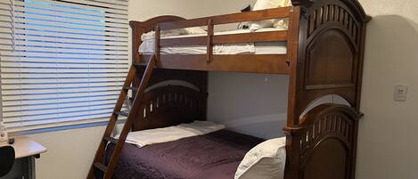A bunk bed with a ladder, a desk, and a window with blinds.